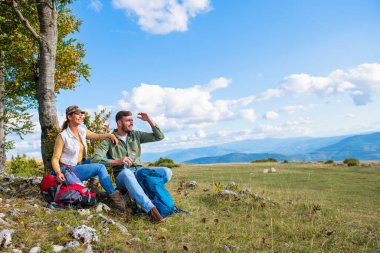 Genç çift dağlarda seyahat ederken kayanın üzerinde dinlenirken su içiyor.