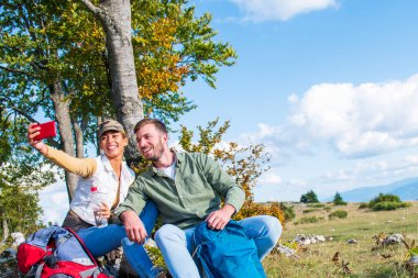 Genç çift dağlarda seyahat ederken kayanın üzerinde dinlenirken su içiyor.