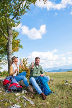 Genç çift dağlarda seyahat ederken kayanın üzerinde dinlenirken su içiyor.