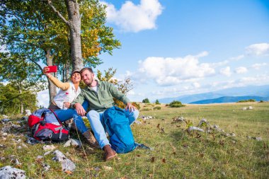 Neşeli genç çift dağlarda seyahat ederken dışarıda selfie çekiyorlar.