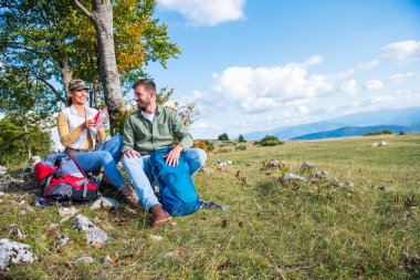 Genç çift dağlarda seyahat ederken kayanın üzerinde dinlenirken su içiyor.