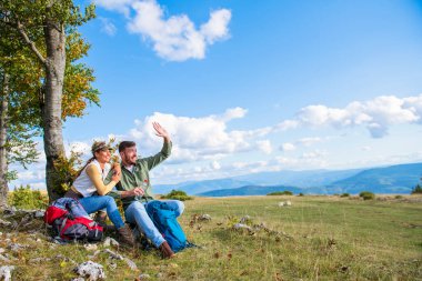 Genç çift dağlarda seyahat ederken kayanın üzerinde dinlenirken su içiyor.