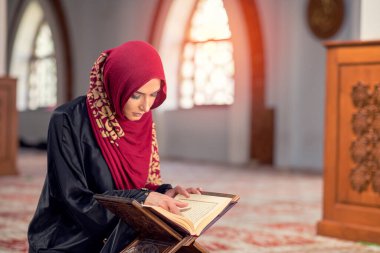 Camide Kur 'an okuyan genç Müslüman kadın ve pencereden düşen güneş ışığı.