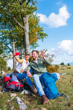 Neşeli genç çift dağlarda seyahat ederken dışarıda selfie çekiyorlar.