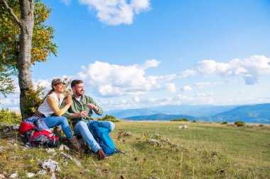 Genç çift dağlarda seyahat ederken kayanın üzerinde dinlenirken su içiyor.