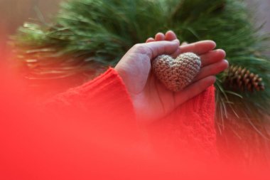 Kadın kırmızı ceketli bir küçük örgü kalp ahşap arka plan üzerinde tutarak. Aşk ve Sevgililer günü kavramı.