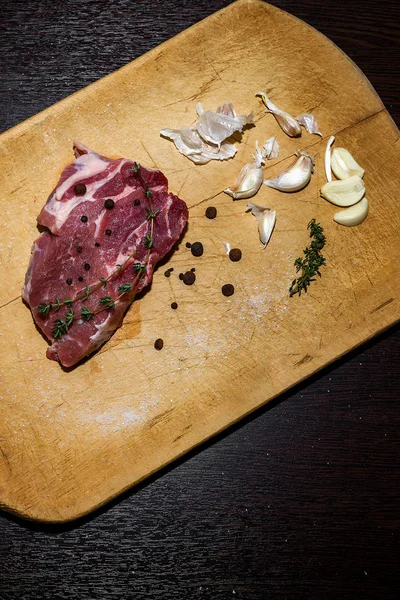 Carne crua marmorizada numa tábua de corte. Em um fundo preto — Fotografia de Stock