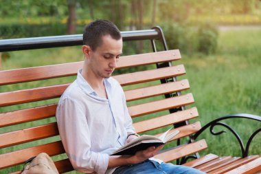 Genç yakışıklı bir adam, bankta oturmuş kitap okuyan bir turist..