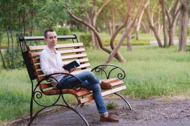 Genç yakışıklı bir adam, bankta oturmuş kitap okuyan bir turist..