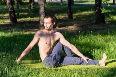 Spor kıyafetleri içinde genç, güzel bir beyaz adam yeşil çimlerin üzerinde, parkta uzanıyor. Yoga ya da fitness dersleri için hazırlık yapın. İzolasyon kipinin ihlali.