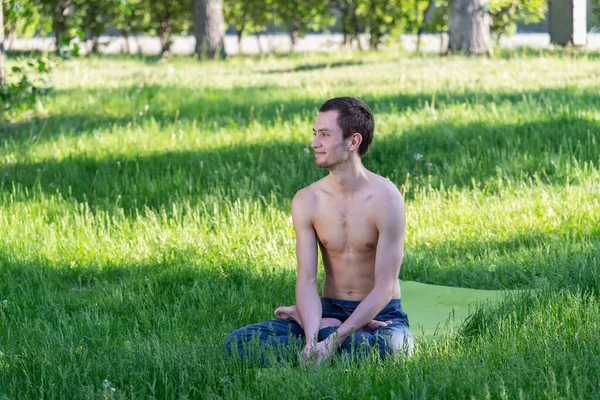Spor kıyafetleri içinde genç, güzel bir beyaz adam yeşil çimlerin üzerinde, parkta uzanıyor. Yoga ya da fitness dersleri için hazırlık yapın. İzolasyon kipinin ihlali.