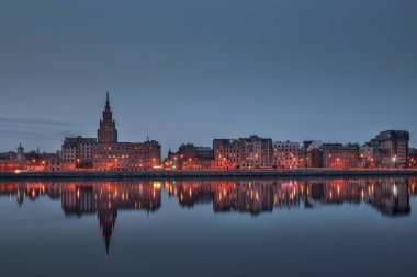 Riga 'daki nehir kıyısında gece görüşü yansıyor.