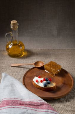 kızarmış ekmek, yoğurt ve meyve, bilberries, yaban mersini ve bal tarak keten kumaş arka plan ve arka plan üzerine şişe ile ahşap bir plaka üzerinde kırmızı kuş üzümü ile tost