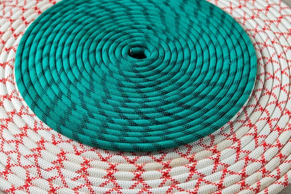 white-red and green rope for mountaineering or sailing in irregularly wound ring on textured fabric background