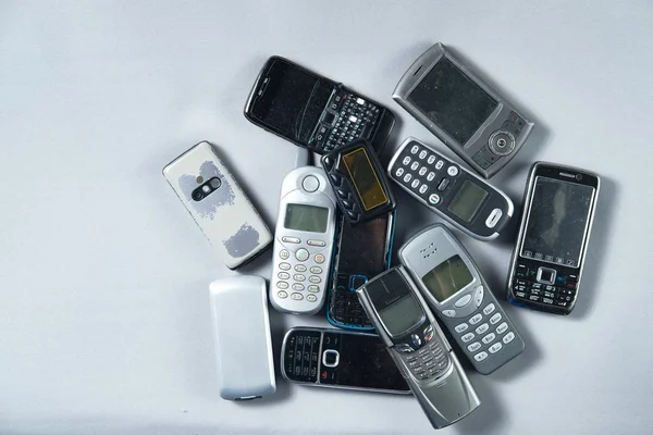 several old mobile phones lie in a pile on a white background