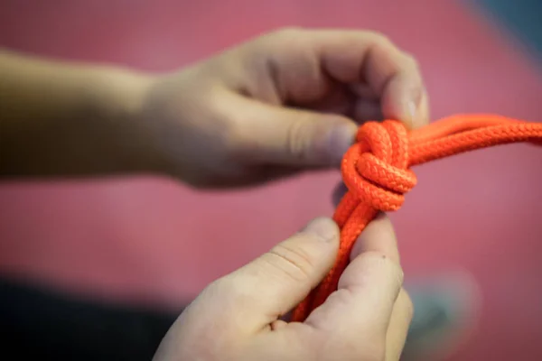 bright orange climbing rope with knots in the hands of a child in green t shirt