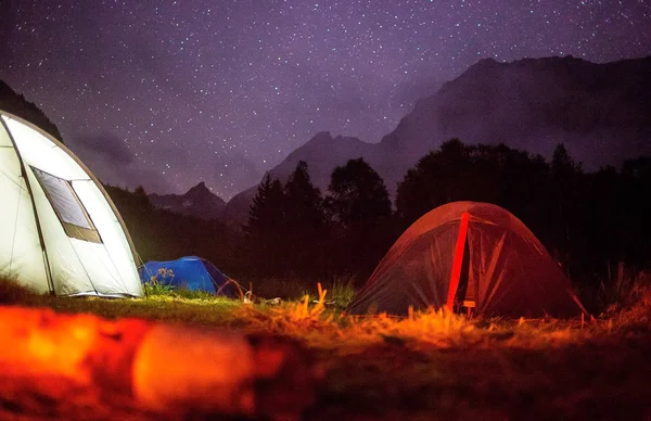 tourist tents are in the meadow at night in the mountains against the starry sky