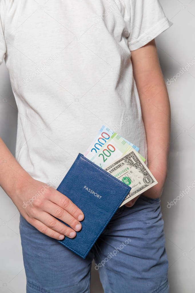 passport with money bills of dollars and new rubles in the hands of a child in a white shirt and blue pants