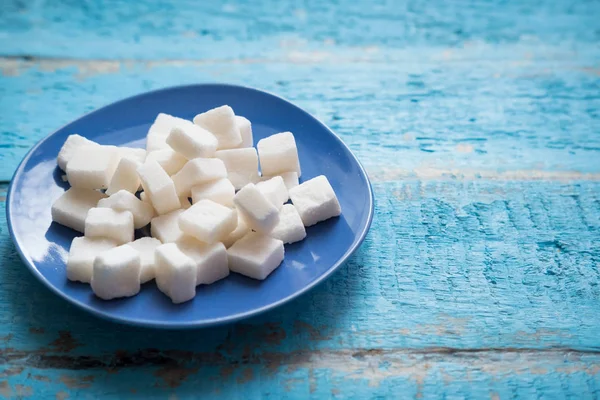 pressed sugar cubes sugar refined in a blue plate standing on a textured wooden surface