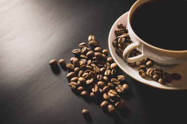 kahve siyah yüzey tablo üzerinde dağınık kavrulmuş kahve çekirdekleri ile beyaz bir bardağa dökülür