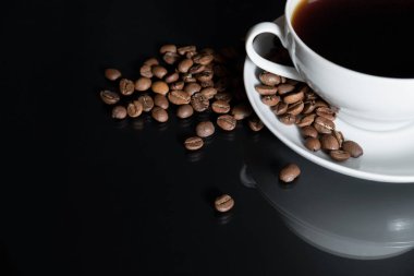 kahve siyah yüzey tablo üzerinde dağınık kavrulmuş kahve çekirdekleri ile beyaz bir bardağa dökülür