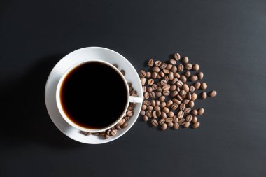 kahve siyah yüzey tablo üzerinde dağınık kavrulmuş kahve çekirdekleri ile beyaz bir bardağa dökülür