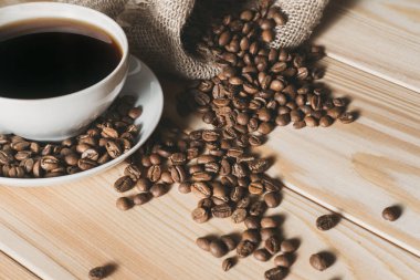 kahve kavrulmuş kahve çekirdekleri bir ahşap yüzeye dağınık ile beyaz bir bardağa dökülür