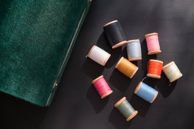 Dikiş kutusu çok çok renkli dikiş ipliği ahşap bobinler üzerinde siyah bir yüzey üzerinde dağılmış