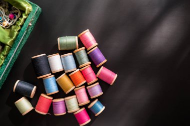Dikiş kutusu çok çok renkli dikiş ipliği ahşap bobinler üzerinde siyah bir yüzey üzerinde dağılmış