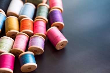 Birçok çeşitli renklerde dikiş ipliği ahşap bobinler üzerinde siyah bir yüzey üzerinde dağılmış