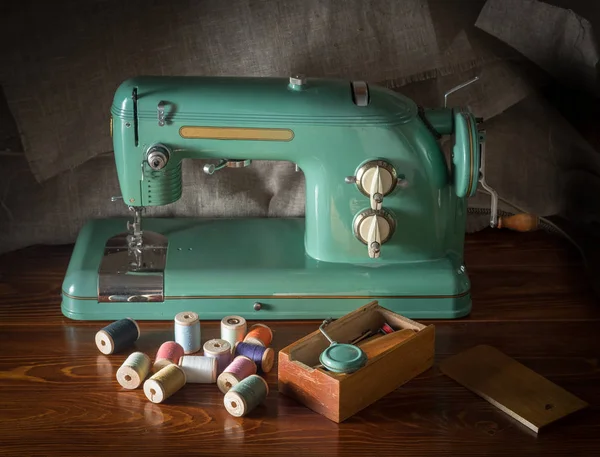一台旧的电动缝纫机 带有工具的盒子和洒有螺纹的线圈 矗立在木制的漆桌上 — 图库照片