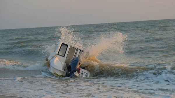 a sunken plastic yacht with a outboard motor beats the waves of the sea on a sandy beach