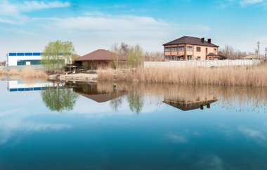 bir göl, mavi gökyüzü bulutlu su bir yansıması ile bahar bir nehir kıyısında evi