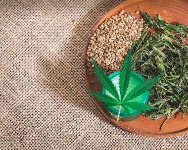 Kenevir kremi kavanozu kuru marihuana ve kenevir tohumlarıyla ahşap bir tabakta duruyor.