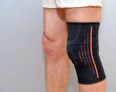 Hafif bir arka planda yaralı bir dizdeki siyah elastik bandaj.