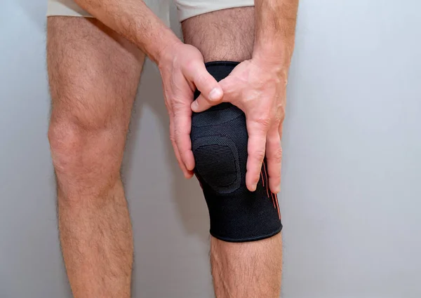 male hands hold knee with black elastic bandage on a light background