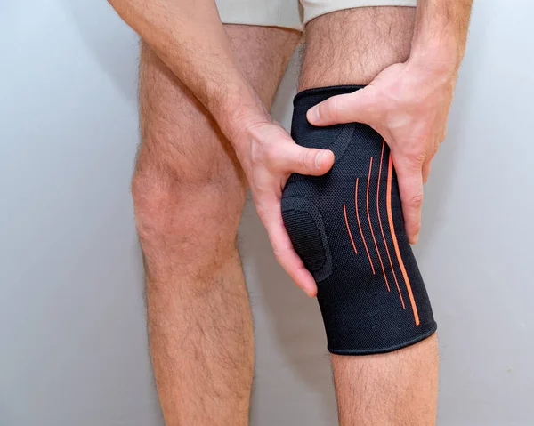 male hands hold knee with black elastic bandage on a light background