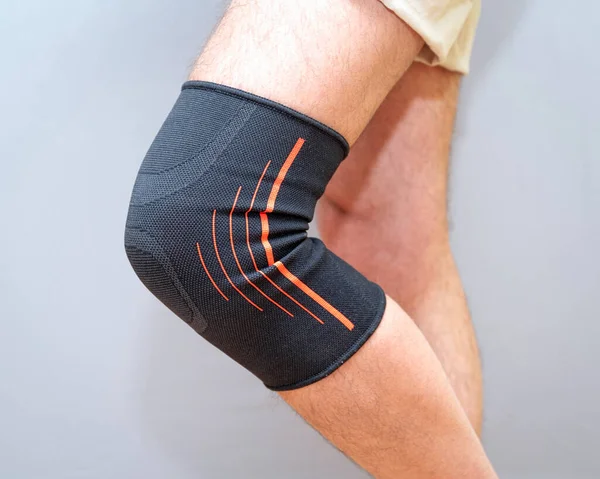 black elastic bandage on an injured knee on a light background