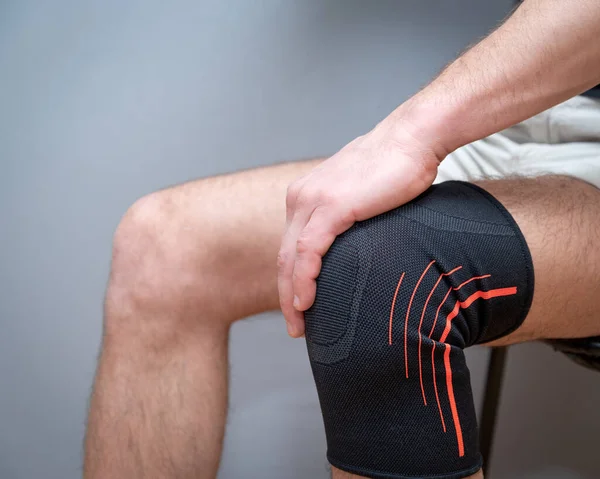 male hands hold knee with black elastic bandage on a light background