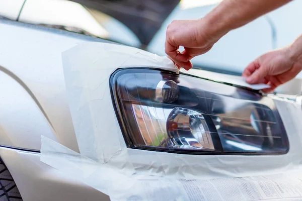 the master seals with adhesive tape a car body for repair of headlights