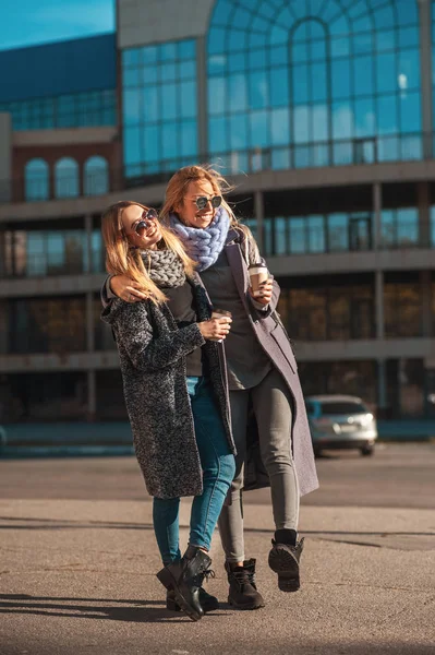 Οι φίλοι με τα πόδια μαζί. Δύο όμορφες γυναίκες που περπατάνε στο δρόμο κρατώντας καφέ χαμογελώντας — Φωτογραφία Αρχείου