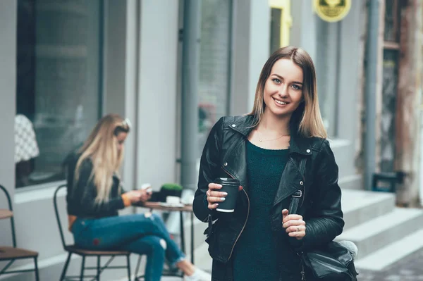 Tira o café. Bela jovem mulher urbana vestindo roupas elegantes segurando xícara de café e sorrindo enquanto caminha ao longo da rua de outono. Pausa para o café depois do estudo. Estilo de vida da moda — Fotografia de Stock