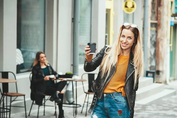 Tira o café. Bela jovem mulher urbana vestindo roupas elegantes segurando xícara de café e sorrindo enquanto caminha pela rua. Pausa para o café depois do estudo. Estilo de vida da moda — Fotografia de Stock