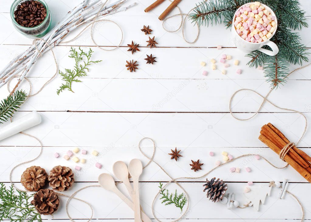Frame composition of cocoa with marshmallow, cinnamon, anise stars, coffee seeds, fir tree, sticks, spoons and ingredients with stuff with copy space on white table. Winter, autumn kitchen, flat lay