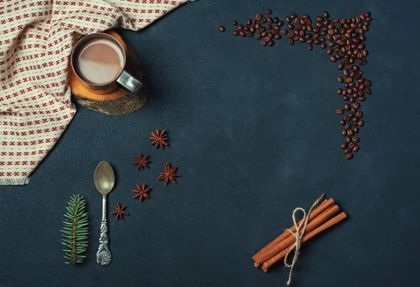 Frame of Cup of Cacao Coffee Beans Cinnamon sticks Spoon and Fir Branch on Dark Texture Table decorated with Napkin. Kitchen Ingredients Winter or Autumn Composition. Flat lay Top view