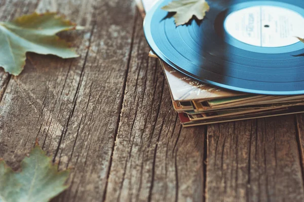 Vintage old vinyl records on wooden autumn background, selective focus decorated with few leaves. Music, fashion, texture, art concepts. pop culture and seasonal objects