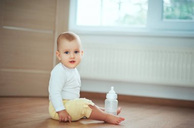 Sevimli küçük bebek şişe süt veya su ile katta yatak odasında oturma ve gülüyor. Bebek çocukluk çocuklar insanlar kavramları. Çocuklu sıcak rahat ev