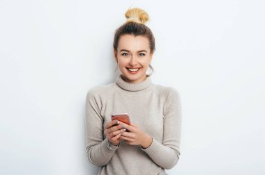 Mutlu neşeli memnun kadın saç topuz çıplak makyaj kapalı arkadaş veya erkek arkadaşı ile sohbet onun smartphone ile kazak duran giyiyor. Yaşam tarzı moda güzellik iş kavramı