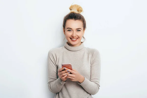 Mutlu neşeli memnun kadın saç topuz çıplak makyaj kapalı arkadaş veya erkek arkadaşı ile sohbet onun smartphone ile kazak duran giyiyor. Yaşam tarzı moda güzellik iş kavramı