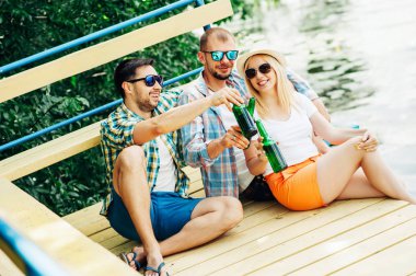 Grup arkadaşları iki erkek ve kadın doğa bira şişesi ile asılı. Sahilde bira ile vakit geçirmek ve eğlenmek! İnsanların duyguları barbekü yaz yaşam tarzı kavramları içecekler